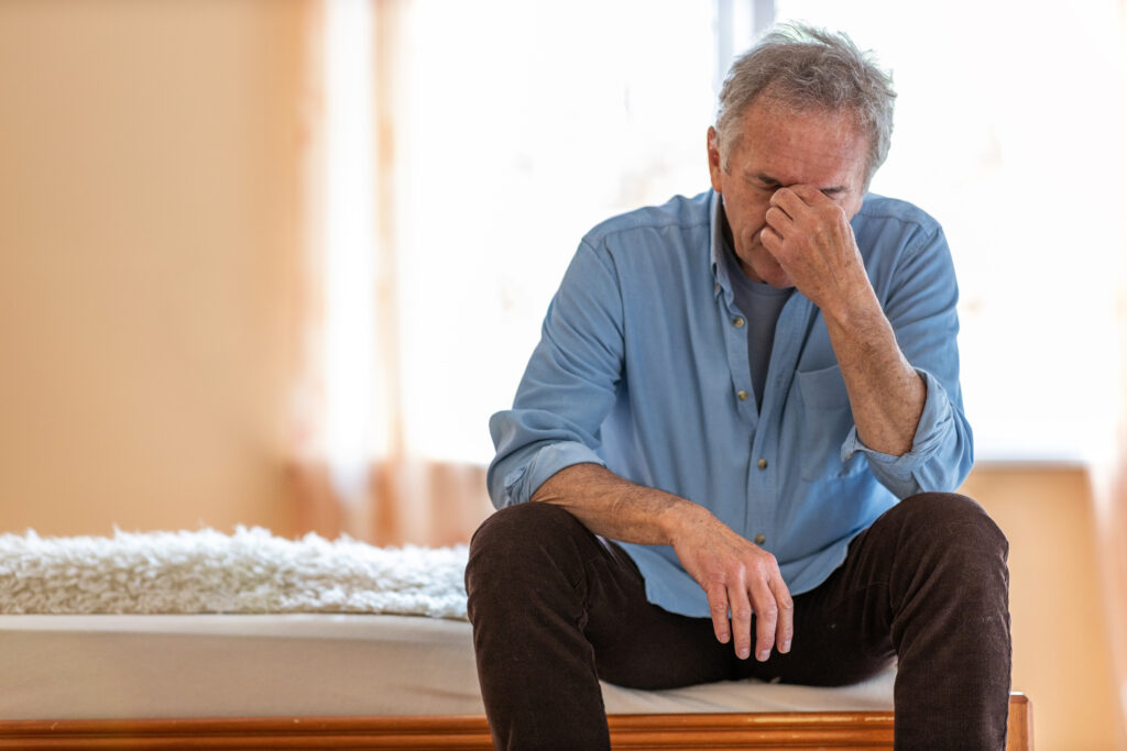 Senior who is depressed sitting on a bed.