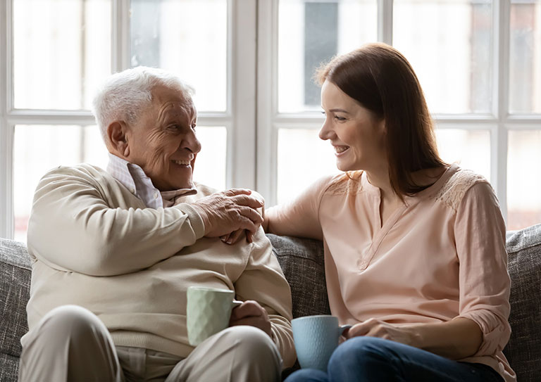 woman talking to dad on couch while drinking coffee