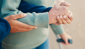 Caregiver holding an older adult’s arm while walking, representing support during an assisted living adjustment.